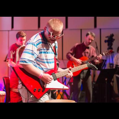 josh playing a red flying-V guitar in a stripey top